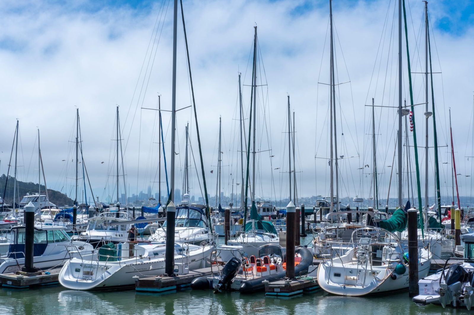 A bustling marina with sailboats and yachts moored under a bright cloudy sky